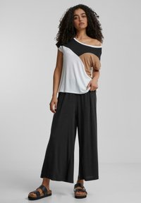 Un pantalon large noir à coupe ample associé à un haut multicolore à manches courtes en segments géométriques noirs, blancs et beige.