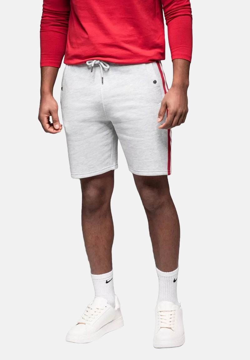 Pantalones cortos de algodón gris claro con rayas rojas en los laterales, con una cintura ajustable y bolsillos frontales, combinados con zapatillas blancas y calcetas de caña corta.