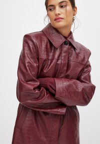 Bordeaux krokodillenembossed leren jas met een grote kraag en knoopsluiting, voorzien van wijde mouwen en een gestructureerde afwerking.