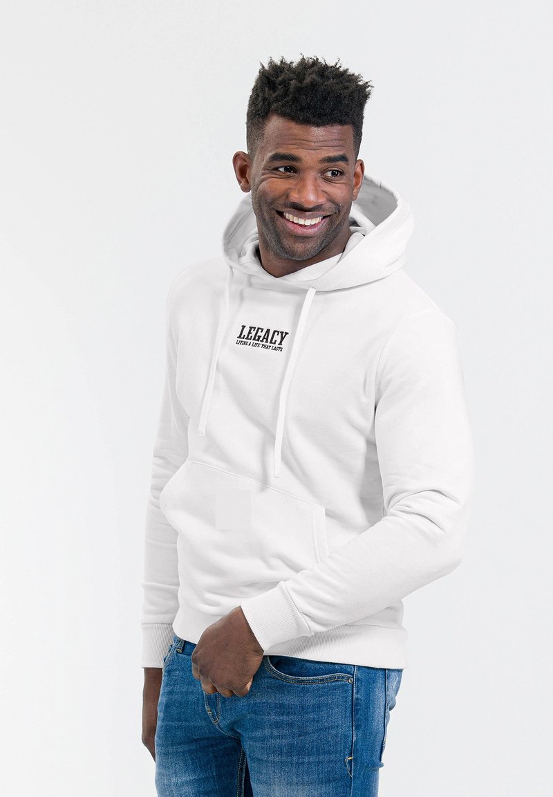 Witte hoodie met een buidelzak, trekkoorden en het logo "LEGACY" op de borst. Gepaard met blauwe denim jeans. Gladstof textuur.
