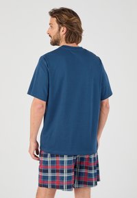 Camiseta de algodón azul marino de mangas cortas, combinada con pantalones cortos de cuadros que presentan cuadrados rojos, azules y blancos. Corte holgado y textura suave.