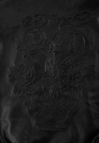 Černý kožený povrch s embossovanými vzory růže, draka a květinových prvků. Text "Ed Hardy" je integrován do designu.