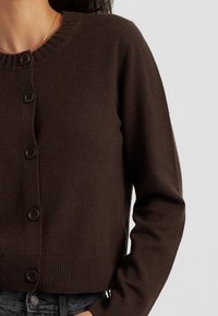 Bruine gebreide cardigan met een ronde halslijn, knoopsluiting, geribbelde zoom en lange mouwen. Zachte textuur met een aansluitende silhoutte.