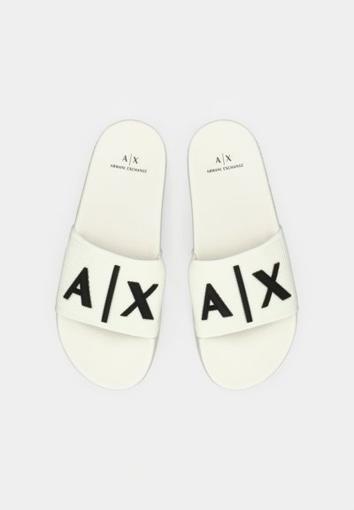 Sandales à glissière blanches avec une sangle texturée. Grandes lettres noires "A/X" imprimées sur la sangle. Design minimaliste avec une semelle plate.