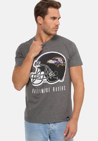 Harmaa lyhythihainen t-paita, jossa on Baltimore Ravens -logo, joka sisältää jalkapallokypärän ja tekstiä. Valmistettu pehmeästä puuvillasekoitekankaasta.