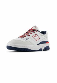 Sneaker en cuir blanc avec des accents rouges et bleu marine, présentant un design texturé, un col rembourré et un logo visible sur le côté.