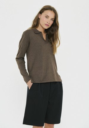 Bruine langmouw polo met v-hals, gedragen met zwarte knielange shorts. De stof lijkt zacht en textuur te hebben, met zijzakken zichtbaar.