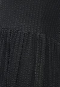 Melna teksturēta kleita ar vertikālām svītrām un krokotu svārku. Materiāls šķiet mīksts ar daudzslāņu izskatu un smalkām rakstām.