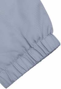 Jasnoszara tkanina z delikatnym wzorem jodełki, wyposażona w elastyczny mankiet i gładką teksturę na krawędzi.