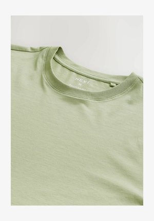 T-shirt en coton vert clair avec un col rond et une texture douce. Présente une étiquette avec "NEXT," taille "M," et "COUPE RÉGULIÈRE" imprimée à l'intérieur.