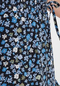 Vestido floral con flores azules, blancas y verdes sobre un fondo negro. Presenta una cintura fruncida y un detalle de lazo. Tejido ligero.