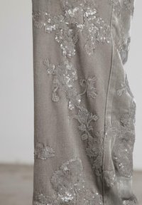 Tela de terciopelo gris con intrincados bordados florales de lentejuelas, que exhibe patrones texturizados detallados y un ligero brillo en una superficie suave.