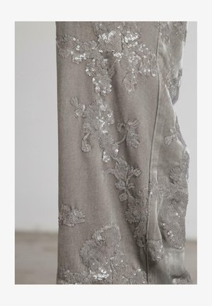 Tela de terciopelo gris con intrincados bordados florales de lentejuelas, que exhibe patrones texturizados detallados y un ligero brillo en una superficie suave.