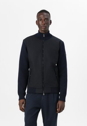 Navy bomber jacket with a high collar, zip front, and ribbed cuffs. Upper body features a smooth fabric, lower part includes textured accents.