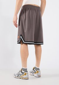 Shorts de sport gris avec des accents noir et blanc, taille élastique et détail d'ouverture sur le côté. Baskets argentées et dorées avec des chaussettes rayées.