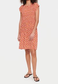 Kukallinen mekko, jossa on smockattu yläosa, lyhyet röyhelöhiha ja levytty hame oranssin, vaaleanpunaisen ja keltaisen sävyissä.