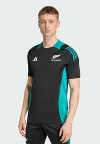 Camiseta deportiva negra con paneles laterales turquesa, con mangas cortas, cuello redondo y acentos de logo en blanco. Fabricada con tejido transpirable.