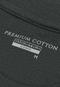 Donkergrijze kledinglabel met de tekst "PREMIUM COTTON," "Intimissimi," "UOMO," en maat "M." De stof ziet er glad uit met nette stiksels.