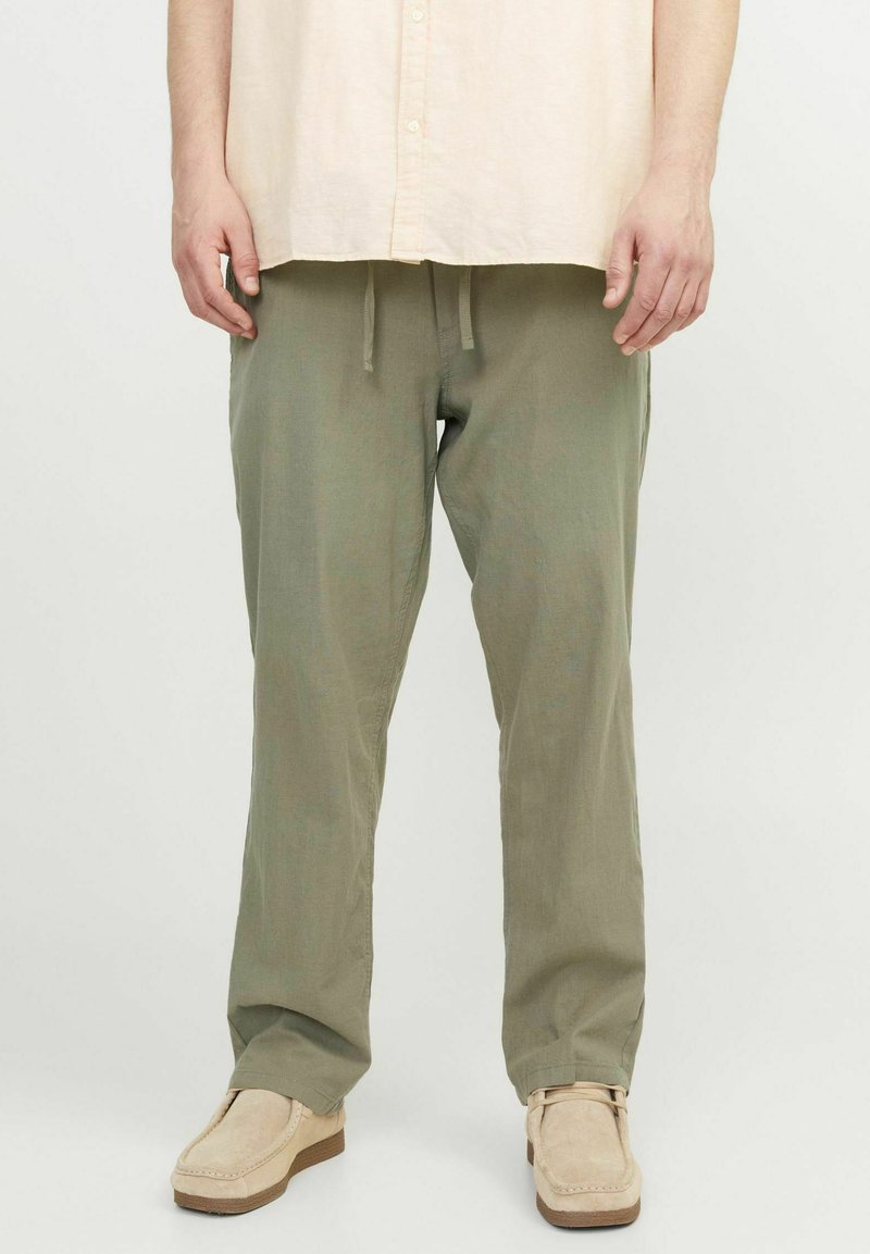 Lichtgroene, losse broek met een trekkoord in de taille, gemaakt van een zachte, gestructureerde stof. Draagt met beige instappers.