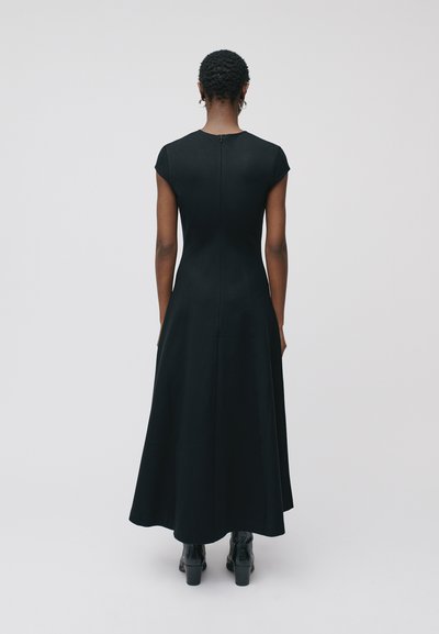 Robe noire ajustée avec des manches courtes, longueur genou, tissu lisse, fermeture éclair au dos, ourlet évasé, assortie à des bottes à talons texturées noires.