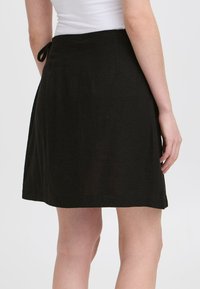 Jupe noire en tissu léger, dotée d'une taille nouée et d'un ourlet évasé, offrant un design simple et épuré.