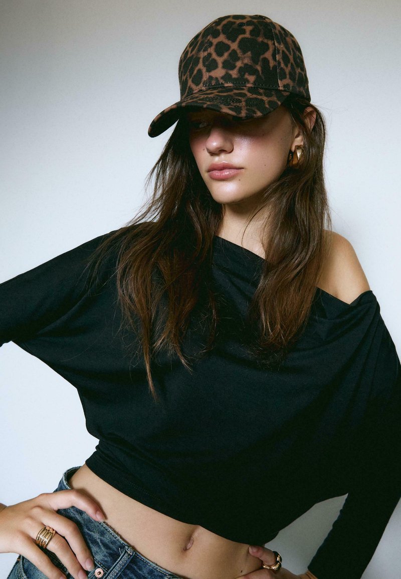 Sort off-shoulder top parret med denim shorts. Brun leopardmønstrede cap med en rund skygge. Guld ring accenter.