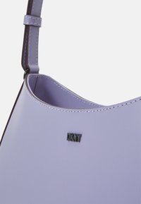 Fioletowa skórzana torebka na ramię z zaokrąglonym kształtem, kontrastowym ciemnym szwem i metką z logo DKNY z boku.