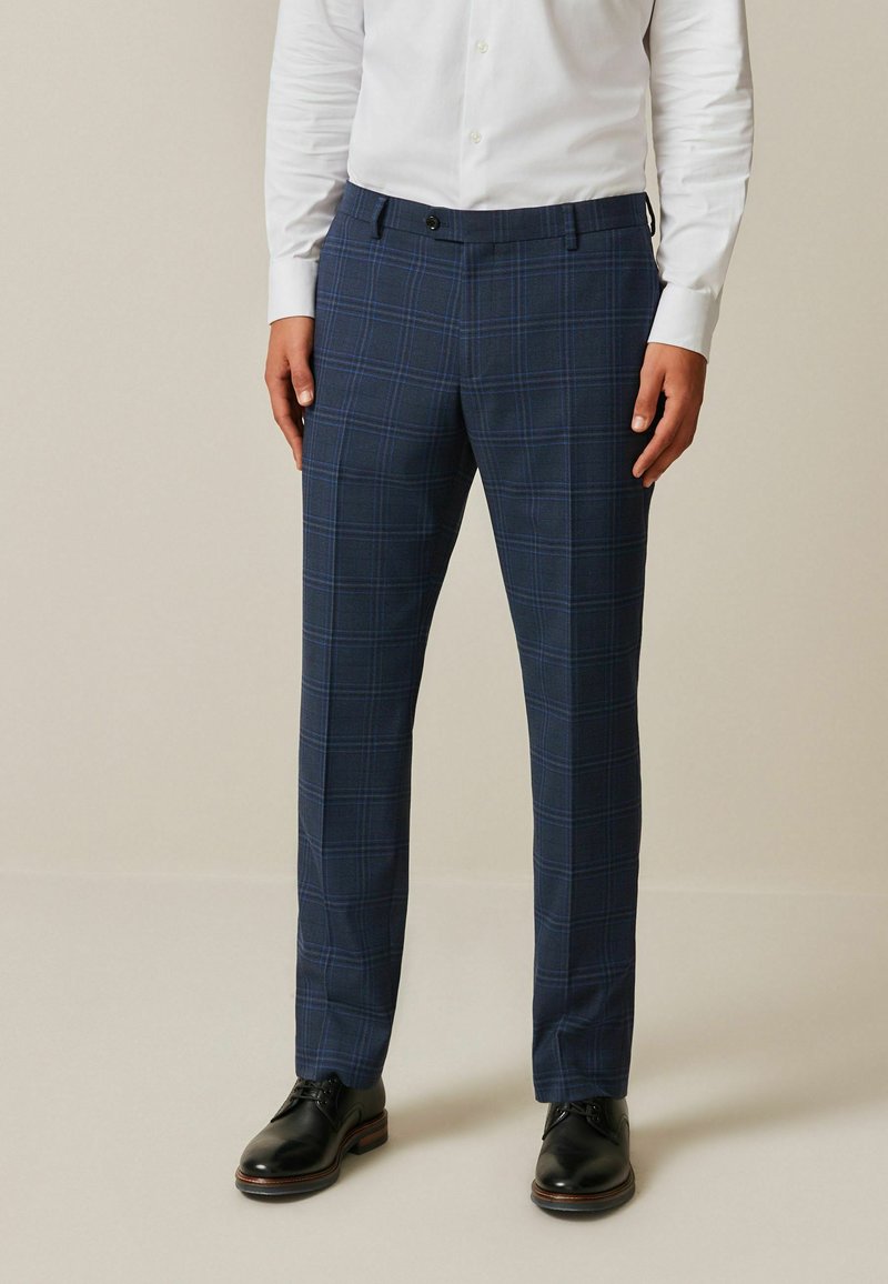 Navy plaid trousers with a subtle check pattern. Tailored fit, made from textured fabric, paired with black lace-up shoes.