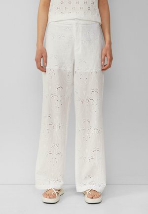 Pantalons brodés blancs et légers avec des motifs floraux découpés et des coutures décoratives, présentant une coupe ample et des poches avant.