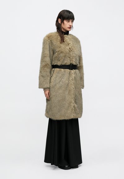 Abrigo de piel sintética en marrón claro con un cinturón negro, con mangas largas y un ajuste ligeramente holgado, combinado con una falda larga negra.