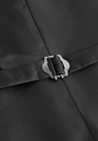 Tela negra con textura y un acabado suave que presenta una hebilla de metal plateado. La hebilla está colocada de manera central, asegurando los paneles de tela entre sí.
