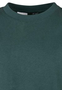 Tamsiai žalia marškinėliai su apvalia iškirpte, su rulonu apdailintu apykakle ir matoma lygių mezginių tekstūra.