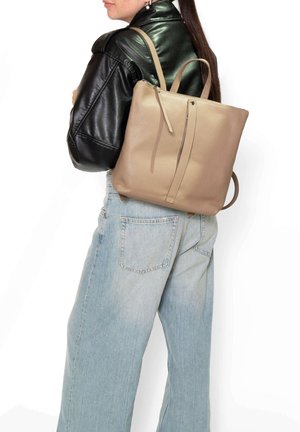 Donna che indossa una giacca di pelle nera e jeans azzurri chiari con uno zaino di pelle beige con dettaglio di cerniera sulla schiena.