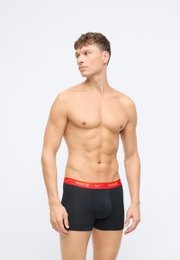 Čierne boxerky s červeným logom Nike na páse, hladká textúra, priliehavý dizajn a krátka dĺžka nohavíc, prezentujúce štíhly tvar.