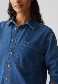 Camicia di jeans blu scuro con colletto a bottoni, taschino frontale e dettagli di cucitura in vista. Tessuto morbido e vestibilità comoda.