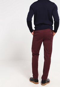 Donkerrode broek met een slanke pasvorm en rechte pijpen, gemaakt van een katoenmix, voorzien van een enkele achterzak en bruine leren schoenen.