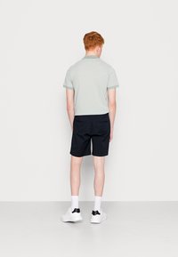 Polo vert clair avec des bordures vertes, assorti à un short noir. Le mannequin porte des baskets blanches avec des accents noirs. Design simple et décontracté.