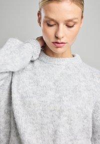 Light grey knit sweater with a round neckline and long sleeves, featuring a soft, textured surface and a relaxed fit.