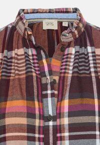 Chemise à carreaux avec col montant boutonné, présentant des rayures marron, orange, rose et blanches, et une étiquette de marque "camel active" taille petite.