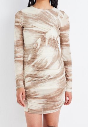 Nainen pukeutunut vartalonmyötäiseen beigeen ja ruskeaan pitkähihaiseen mekkoon, jossa on abstrakti siveltimenvetokuvio, rypytyksiä ja pyöreä pääntie.