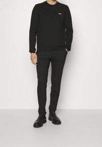 Sweat-shirt noir à encolure ronde avec un petit logo blanc « BOSS », associé à un pantalon noir slim et des bottines noires. Texture lisse.