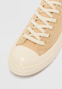 Beige canvas sneaker med en blank creamgummi tåhätta, creamfärgade snören och guldögon. Har en strukturerad sula och sydda detaljer.