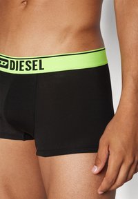 Black boxer shorts with a bright neon green elastic waistband featuring the word "DIESEL" in black lettering. Smooth fabric, fitted design.