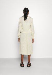 Kermansop dress with black polka dots, long sleeves, a collar, and a fitted waist. Cut below the knee with a soft texture and slight sheen.
