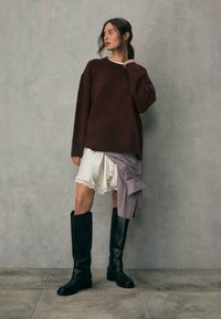 Bordeaux oversized sweater, creme nederdel med blondekant, stribede detaljer og høje sorte læderstøvler. Glat tekstur, afslappet pasform.