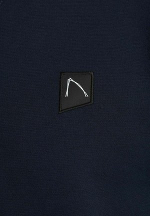 Marinblå stickad tyg med en svart rektangulär patch som har en vit grafisk design. Slät textur och minimalistik estetik.