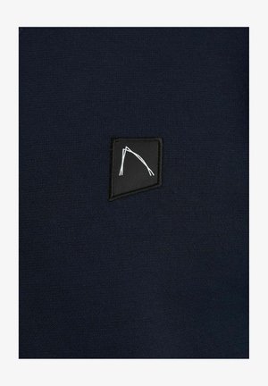 Marineblau gestrickter Stoff mit einem schwarzen rechteckigen Patch, der ein weißes grafisches Design zeigt. Glatte Textur und minimalistisches Ästhetik.