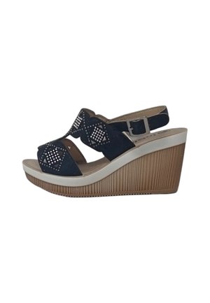 Sandali zeppa in camoscio blu navy con punta chiusa, ritagli decorativi e borchie argentate. Presentano una piattaforma ondulata beige e una fascia regolabile alla caviglia.