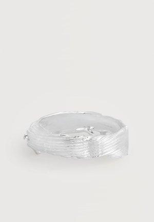 Βραχιόλι μπράτσου από ασημί με υφή, με κυματοειδές ανάγλυφο μοτίβο και γυαλιστερό πολυτελές φινίρισμα σε απλό φόντο.