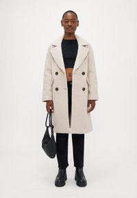 Ανοιχτό μπεζ διπλόχρωμο παλτό με υφή από αφράτο υλικό, διαθέτοντας γιακα κολάρο και σκούρους καφέ κουμπιά. Συνδυασμένο με μαύρα παντελόνια και μπότες.